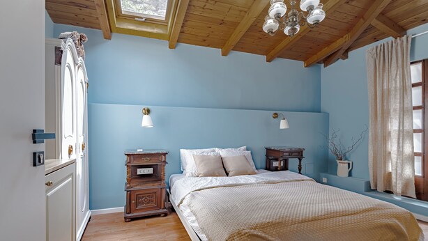 A bedroom with a wooden ceiling, a large bed with white bedding, two bedside tables, and a window with curtains. - The Vlasta Collection Rooms (Zagreb)