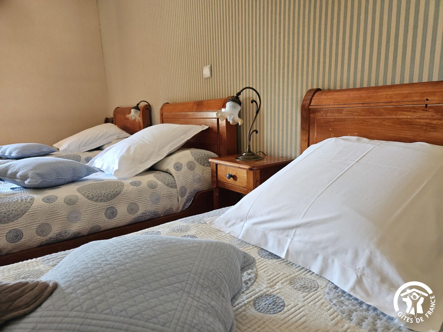 A hotel room with two beds, each with a wooden headboard, a bedside table with a lamp, and a striped wall.