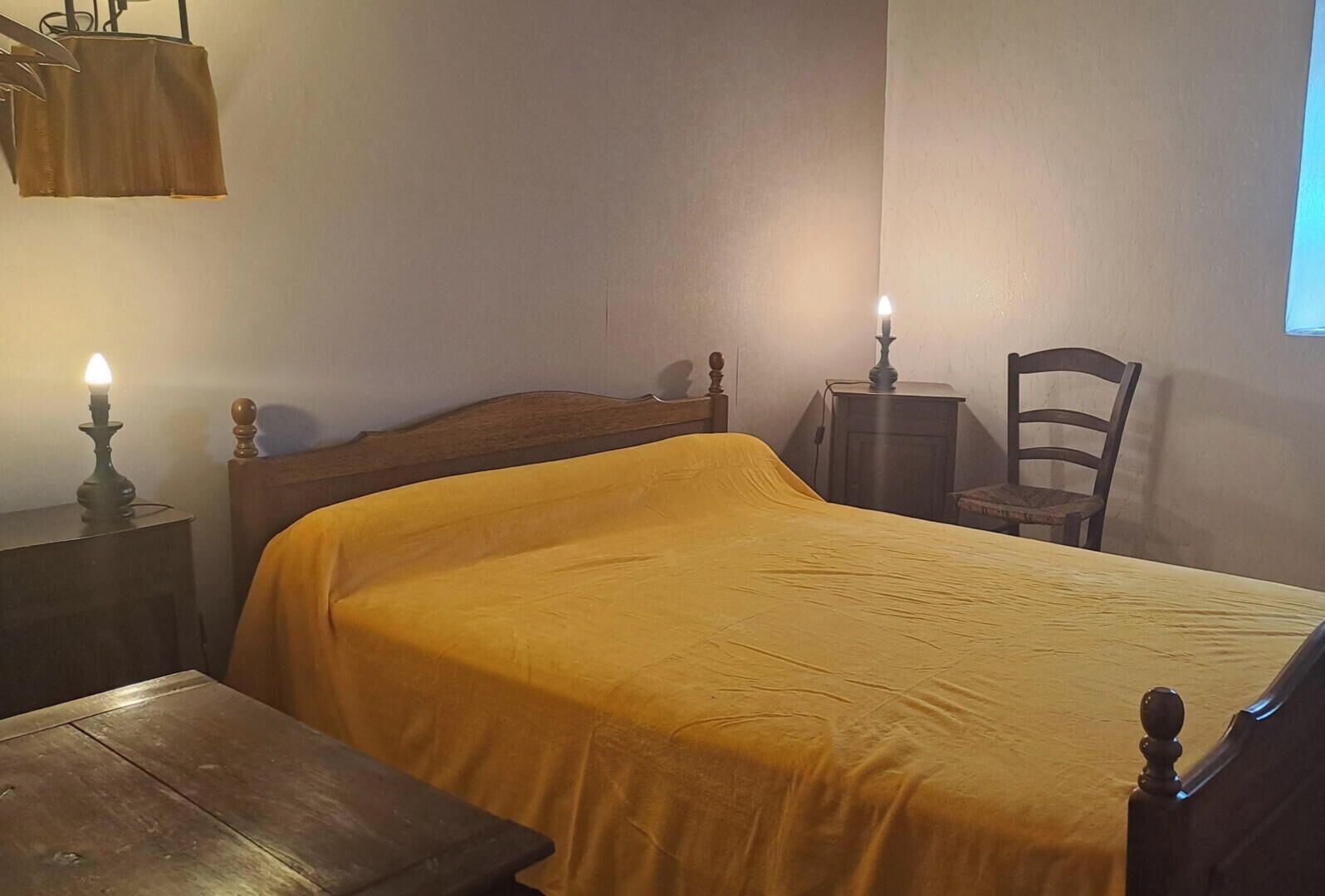 Ein Zimmer mit einem Bett, einem Nachttisch aus Holz, einem Stuhl und einem Fenster.