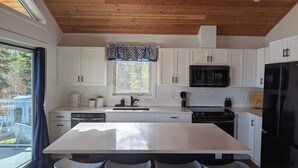 A modern kitchen with white cabinets, a black refrigerator, and a large island with bar stools.