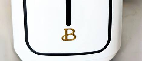 Un electrodoméstico blanco con detalles negros y un toque dorado, que presenta un logotipo de 'B' destacado.
