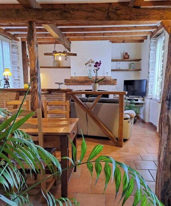 A rustic interior with exposed wooden beams, a wooden dining table, a sofa, and a television.