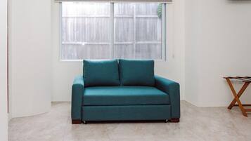 A teal sofa in a room with a large window, a wooden table, and a tiled floor.