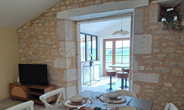 A dining area with a stone wall, a television on a wooden stand, and a table set for two with plates, glasses, and cutlery.