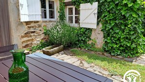 A stone building with ivy-covered walls, a wooden table with a green bottle, and a stone planter with flowers.