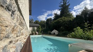 A swimming pool with a stone wall on one side and a wooden deck in the foreground.