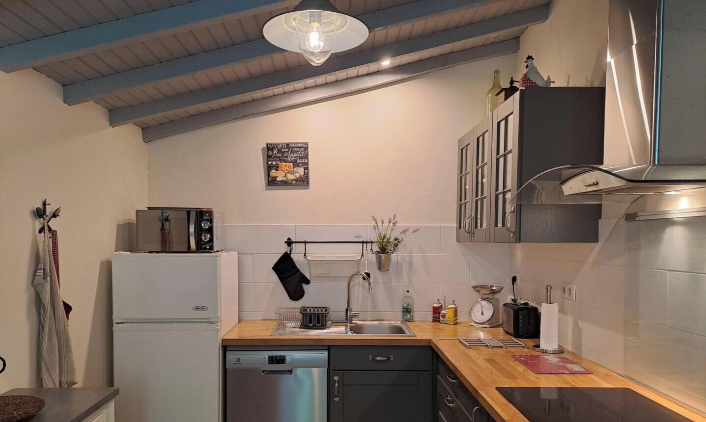 Een compacte keuken met een vaatwasser, een spoelbak en een kookplaat. Boven de spoelbak hangt een pannendroger en boven de kookplaat is een klein raam.
