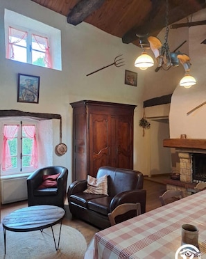 A cozy living room with a fireplace, leather chairs, a wooden cabinet, and a dining table.