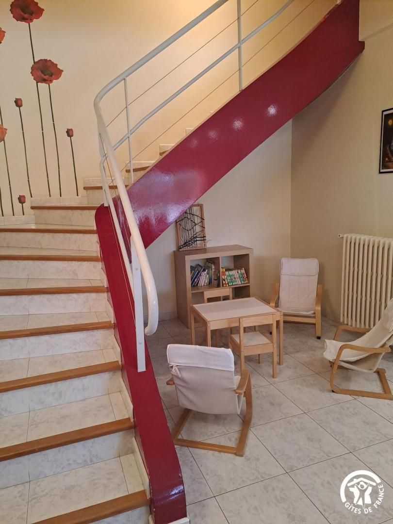 Un escalier avec une rampe rouge mène à un palier. On y trouve deux chaises et une petite table.