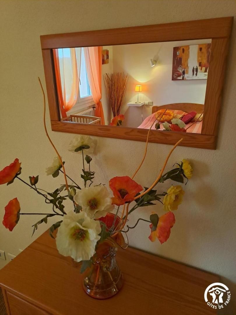 Un miroir accroché au mur, un vase rempli de fleurs et une commode en bois.