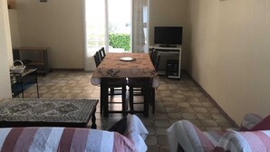 A room with a dining table, chairs, a TV, and a sofa.