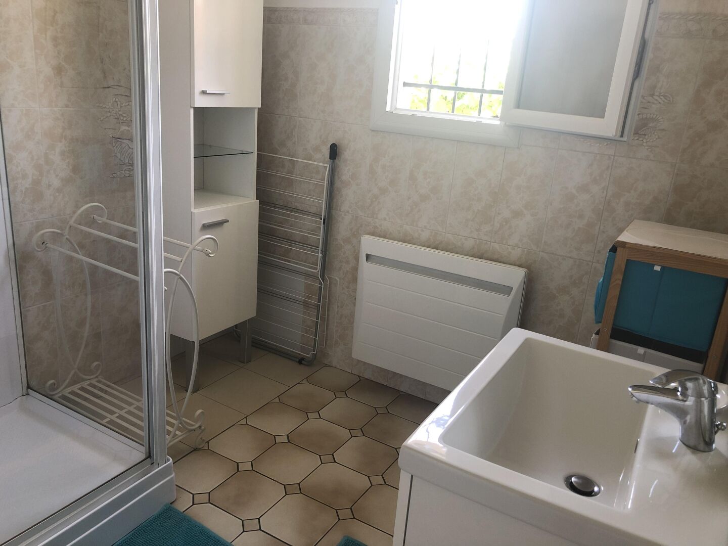 Une salle de bain avec une douche, un lavabo, une fenêtre et un porte-serviettes.