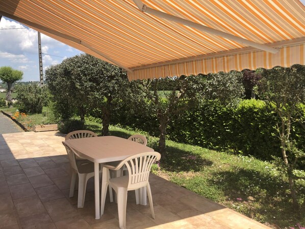 An outdoor patio with a table and chairs, surrounded by greenery and a striped awning. - Peyrat - LESCURE -D'ALBIGEOIS (LESCURE -D'ALBIGEOIS)