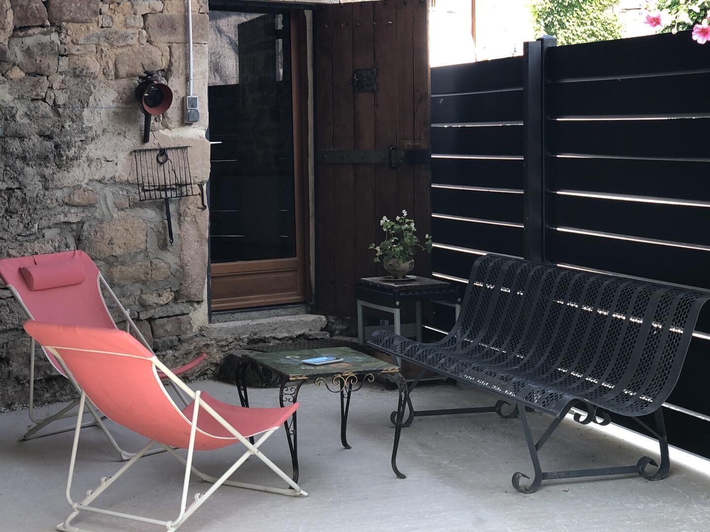 Une terrasse avec un fauteuil de relaxation rouge, un banc en métal noir et une petite table sur laquelle est posée une plante en pot.