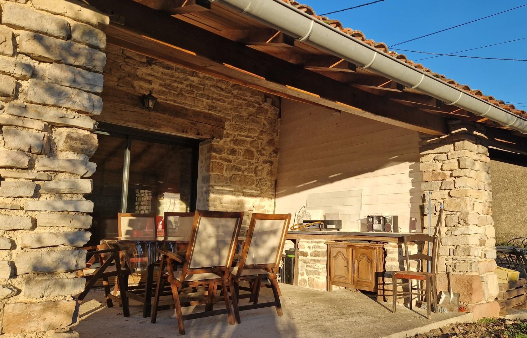 Un edificio de piedra con terraza de madera, asientos al aire libre y techo de tejas.