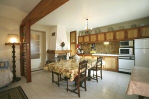 Une cuisine avec des meubles de rangement en bois, une table à manger, des chaises, un lustre et un réfrigérateur.