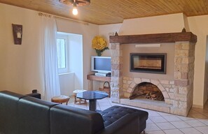 Ein gemütliches Wohnzimmer mit Kamin aus Stein, einem Fernseher auf einer Holzregal und einem Ledersofa.