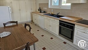 Een kleine keuken met witte kastjes, een houten tafel en een raam met gordijnen.