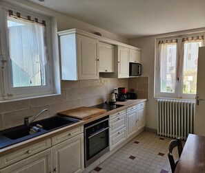 Une cuisine compacte avec des meubles blancs, un four à micro-ondes, une machine à café et un plan de travail en bois.
