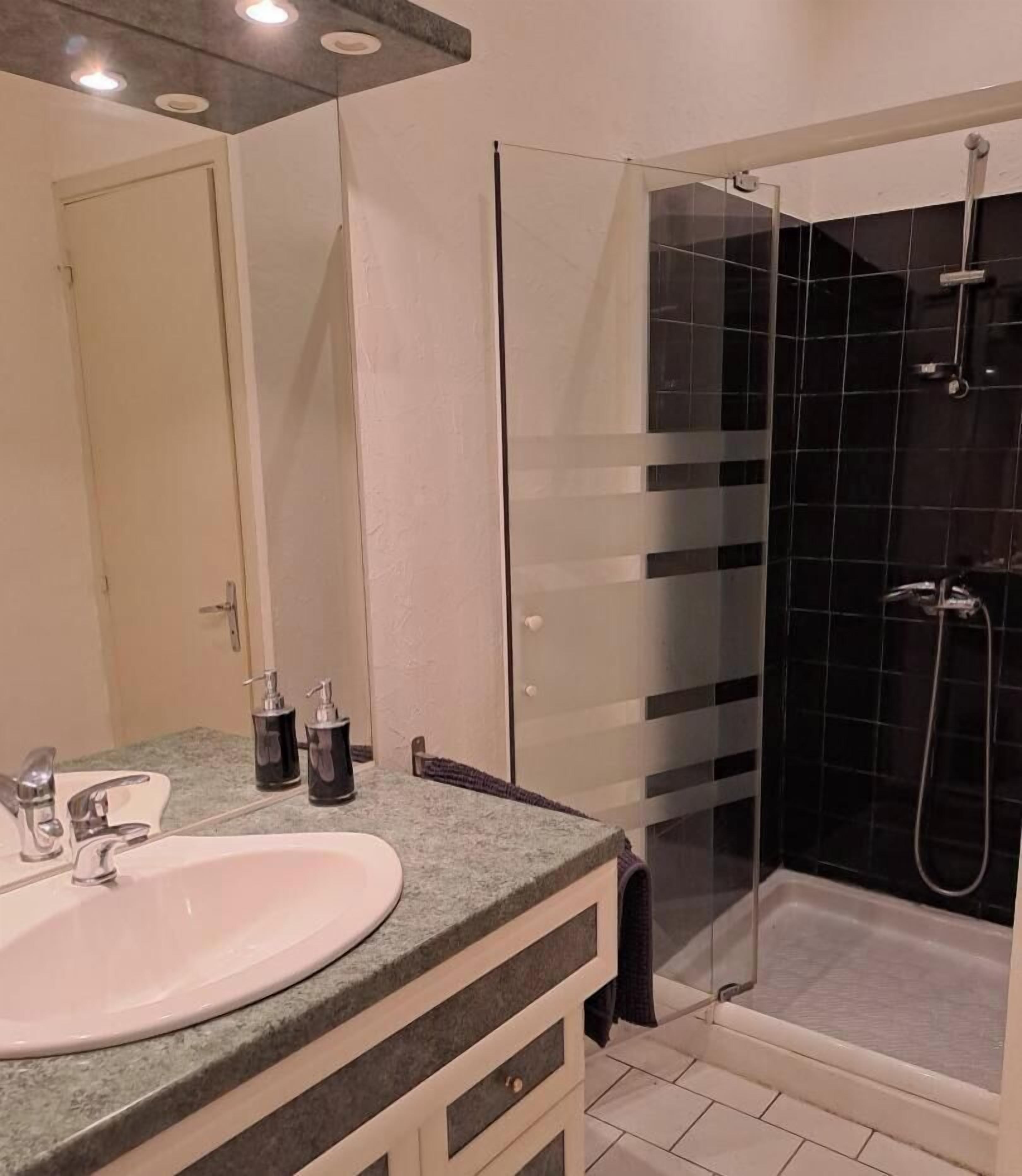 Uma casa de banho com cabine de duche em vidro, lavatório com espelho e um porta-toalhas.