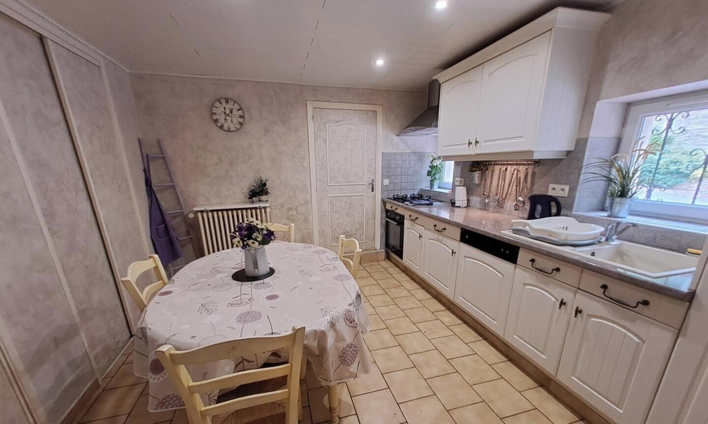 A kitchen with white cabinets, a dining table with chairs, a clock on the wall, and a window with a view.