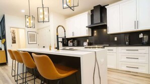Een moderne keuken met witte kasten, een centraal eiland met barkrukken, hanglampen en een zwarte afzuigkap.