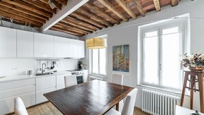 A modern kitchen with white cabinets, a wooden dining table, and a large window.
