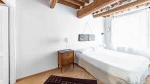 A bedroom with a wooden ceiling, a bed, a nightstand, a lamp, and a rug.
