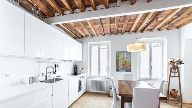 A modern kitchen with white cabinets, a wooden ceiling, and a dining area with a table and chairs.