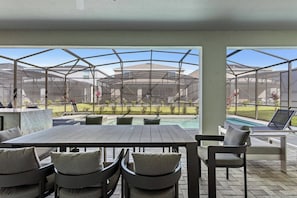 Un patio exterior con mesa y sillas, una piscina y vistas a una zona residencial.