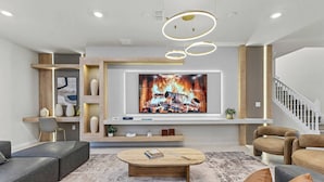 A modern living room with a large flat-screen TV, leather sofas, a wooden coffee table, and a staircase.