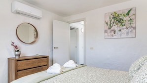 A bedroom with a bed, a wooden dresser, a round mirror, and a painting of plants on the wall. - Home2Book Country Stay with Terrace & BBQ (Las Palmas de Gran Canaria - Cuenca del Guiniguada)