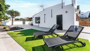 A modern house with a white exterior, a black door, and a small patio with two black lounge chairs. - Home2Book Country Stay with Terrace & BBQ (Las Palmas de Gran Canaria - Cuenca del Guiniguada)