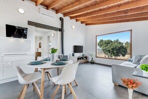 A modern kitchen with white cabinetry, a dining area with white chairs and a round table, a large window with a view of trees, and a grey sofa with a plant. - Home2Book Country Stay with Terrace & BBQ (Las Palmas de Gran Canaria - Cuenca del Guiniguada)
