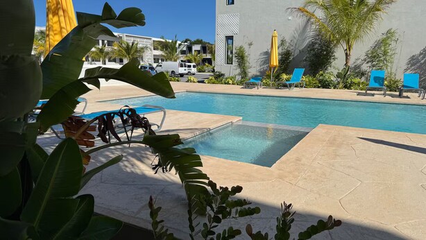 Ein Poolbereich mit Liegestühlen, ein Gebäude im modernen Stil und tropische Pflanzen.