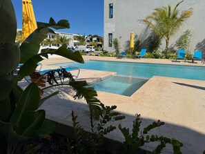 A pool area with lounge chairs, a building with a modern design, and tropical plants.