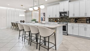 A modern kitchen with white cabinets, a large island with bar stools, and stainless steel appliances.