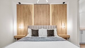 A modern bedroom with a large bed, wooden headboard, bedside tables, and wall-mounted lighting.