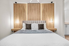 Un dormitorio moderno con una cama grande, cabecera de madera, mesitas de noche e iluminación empotrada.