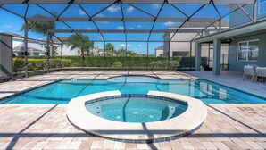 A swimming pool with a hot tub, covered patio area, and a view of surrounding houses.