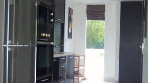 A modern kitchen with black cabinetry, a stainless steel refrigerator, and a built-in oven. - Twin Sands Private Apartment, Phuket (Patong)