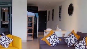 A modern living room with a yellow sofa, a purple sofa, and a white coffee table. There is a ceiling fan, a white ceiling, and a patterned rug. - Twin Sands Private Apartment, Phuket (Patong)