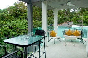 A covered outdoor seating area with a table and chairs, overlooking a swimming pool and lush greenery. - Twin Sands Private Apartment, Phuket (Patong)