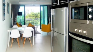 A modern kitchen with a refrigerator, oven, and microwave. There is a dining area with a table and chairs. - Twin Sands Private Apartment, Phuket (Patong)