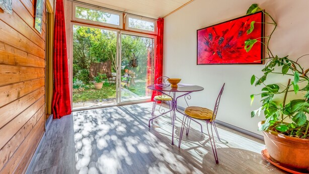 A room with a wooden wall, a glass door, a table with chairs, a potted plant, and a painting. - Holiday Home 'Gîte - Le Samiege' with Private Terrace, Shared Garden and Wi-Fi (Goudargues)