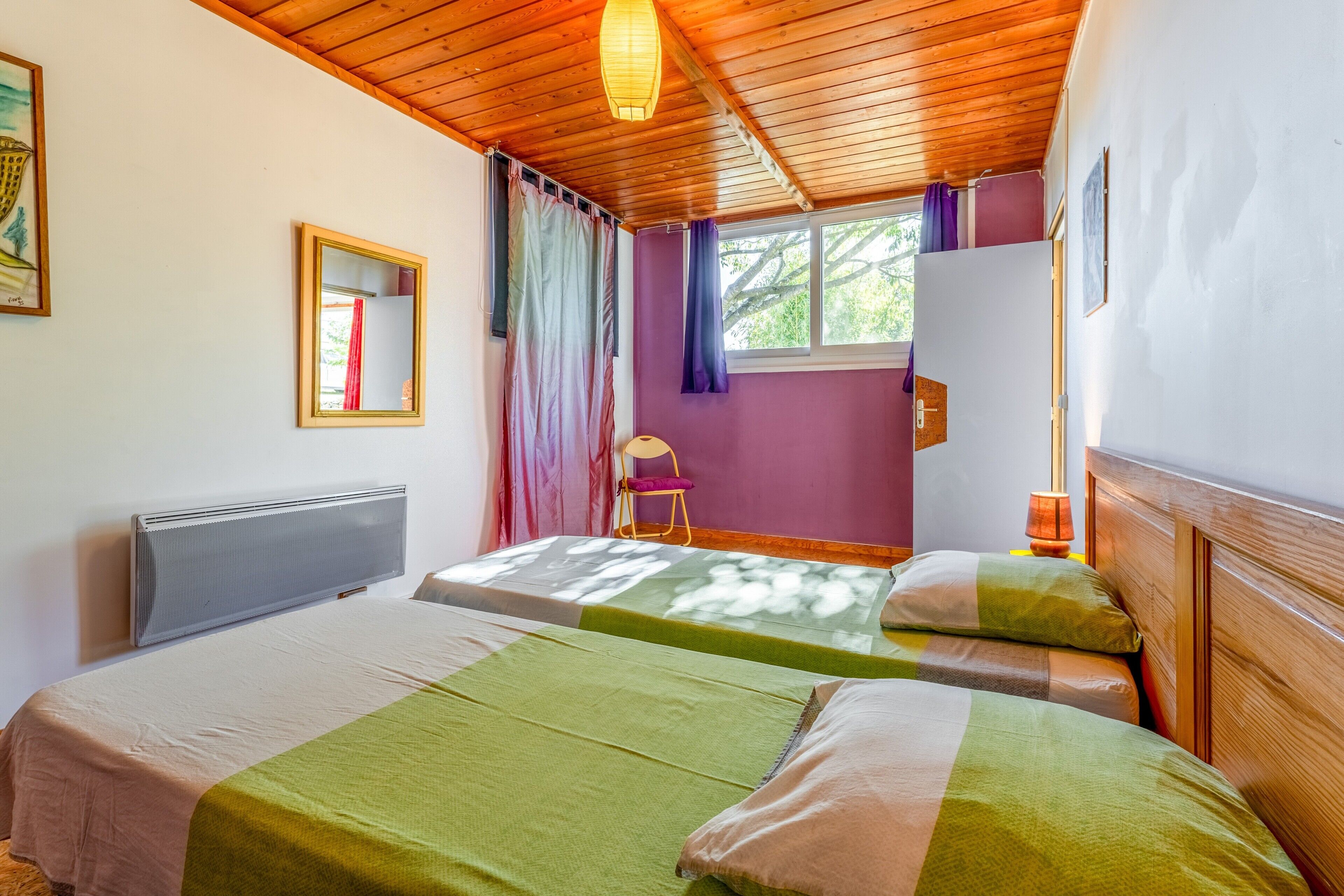 Una habitación con dos camas, una ventana con cortinas, un radiador y una silla.