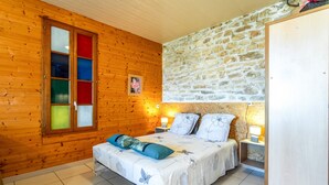 A wooden-paneled room with a bed, a stone wall, and a window with colored glass panes. - Holiday Home 'Gîte - Le Samiege' with Private Terrace, Shared Garden and Wi-Fi (Goudargues)
