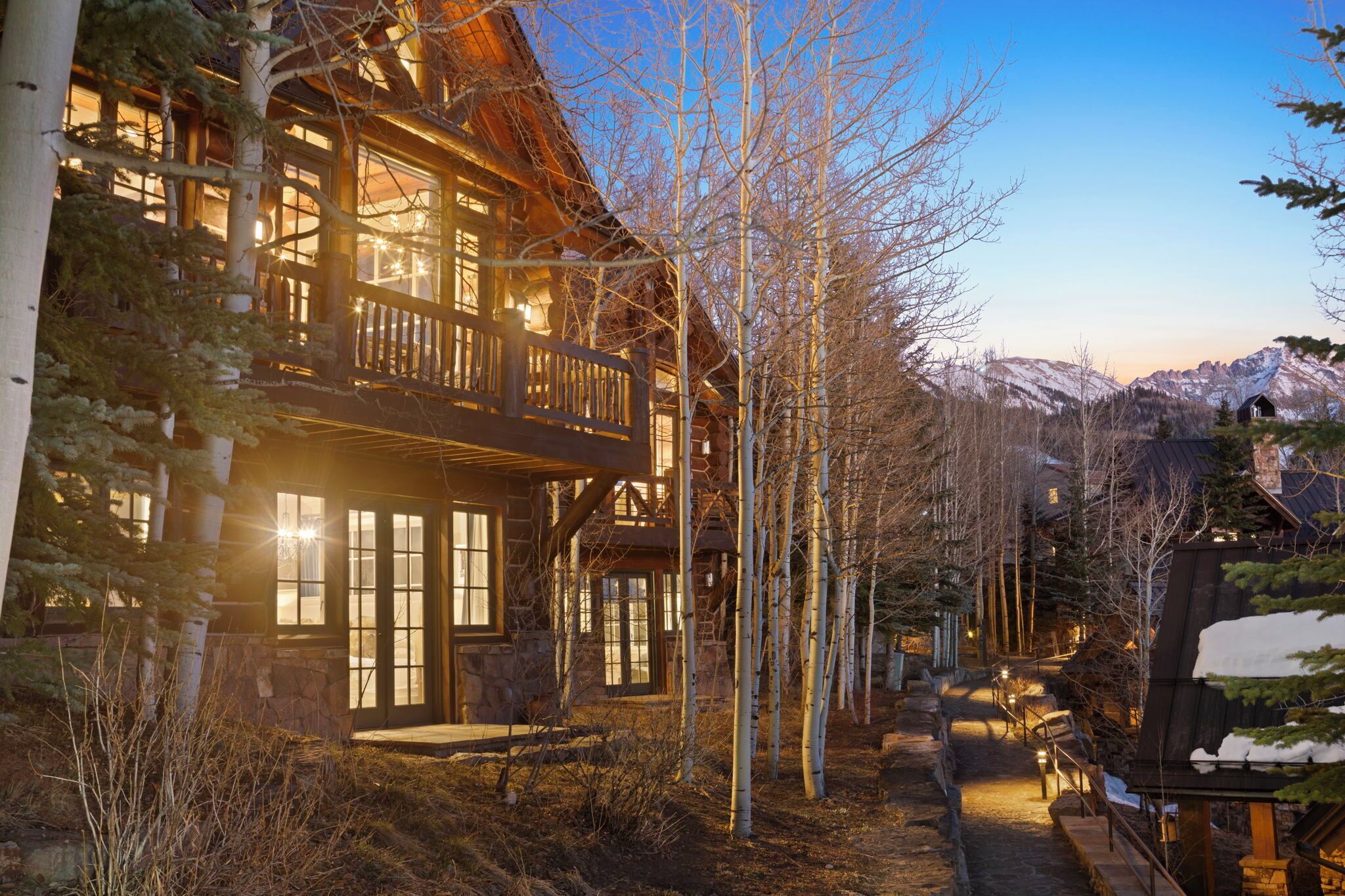 Une cabane en rondins dotée d’un balcon, entourée d’arbres et avec une chaîne de montagnes en toile de fond.