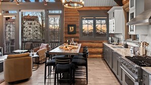 Une cuisine spacieuse dotée d’un grand îlot central, de poutres en bois et offrant une vue sur l’extérieur.