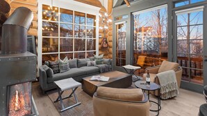 L’intérieur chaleureux d’un chalet en bois, avec une cheminée, un canapé, une table basse et de grandes fenêtres donnant sur l’extérieur.